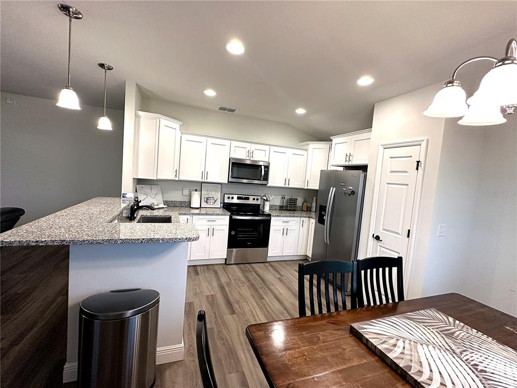 A kitchen features white cabinets, granite countertops, stainless steel appliances, and wood-look flooring — 16951 SW 43RD COURT ROAD, OCALA, FL