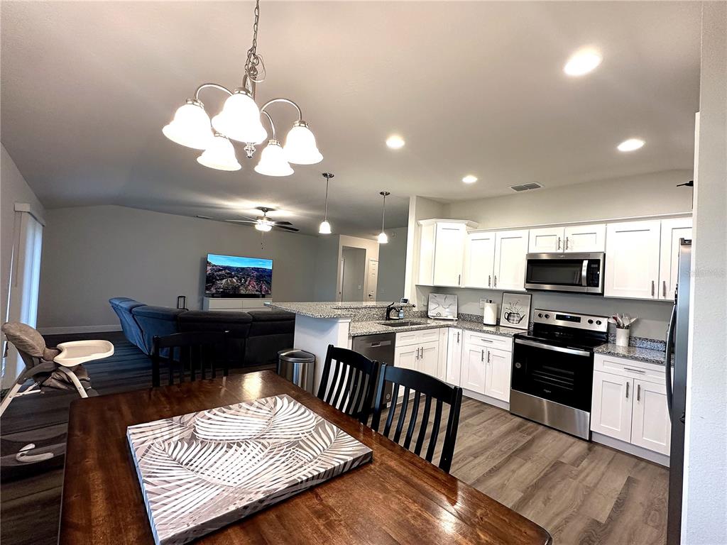 An open-concept kitchen and dining area features white cabinets, stainless steel appliances, and wood-look flooring — 16951 SW 43RD COURT ROAD, OCALA, FL