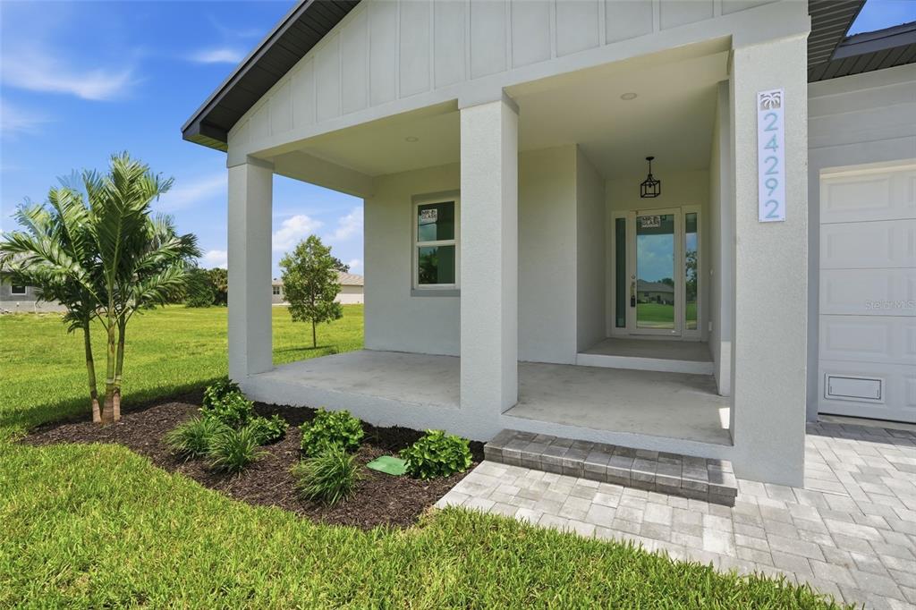 A light-colored house exterior features a covered front porch, a glass-paneled door, and landscaping — 24292 PEPPERCORN ROAD, PUNTA GORDA, FL