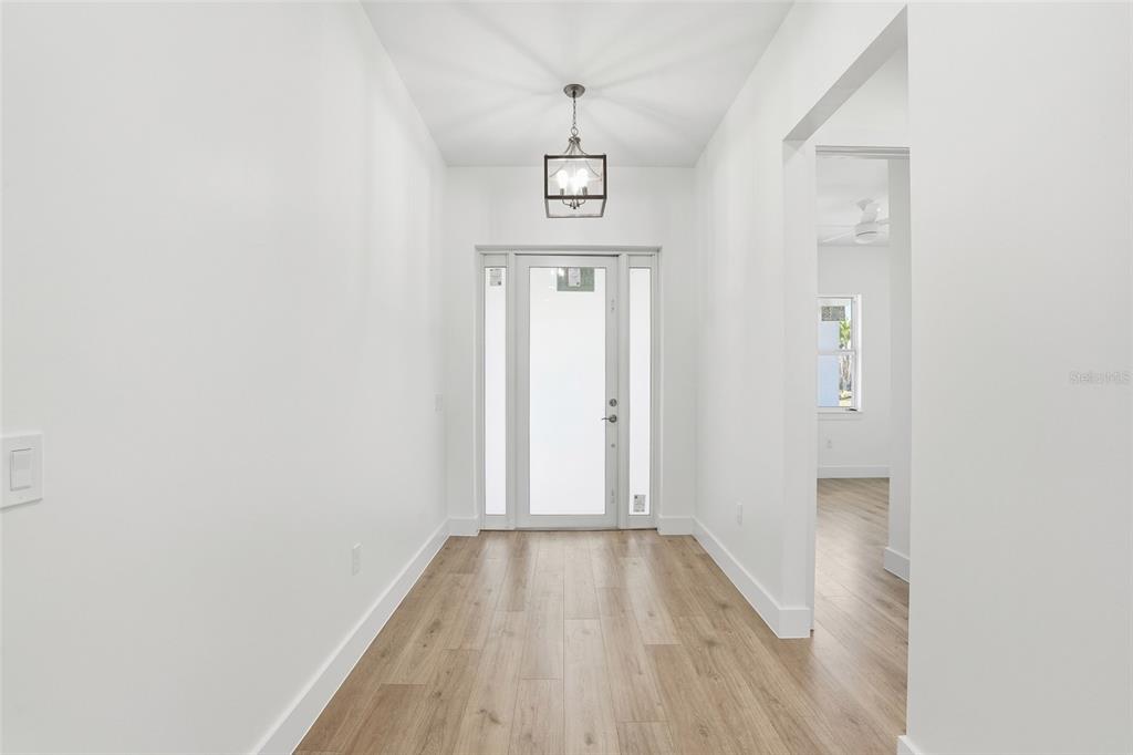 A bright entryway features white walls, light wood-look flooring, and a modern lantern-style pendant light — 24292 PEPPERCORN ROAD, PUNTA GORDA, FL