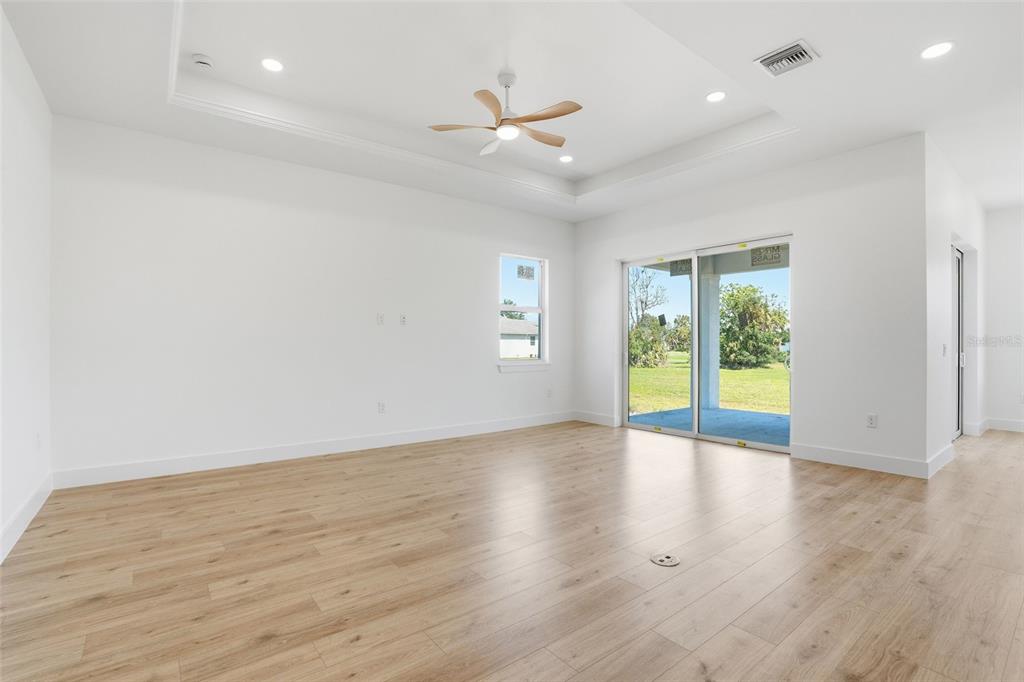 A bright living room features light wood-look flooring, a tray ceiling, and sliding glass doors — 24292 PEPPERCORN ROAD, PUNTA GORDA, FL