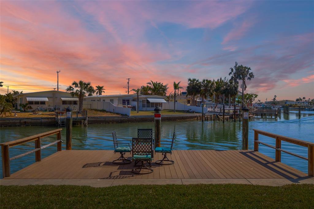 A wooden dock with patio furniture overlooks a canal at sunset near waterfront homes — 145 116TH AVENUE UNIT 301, TREASURE ISLAND, FL
