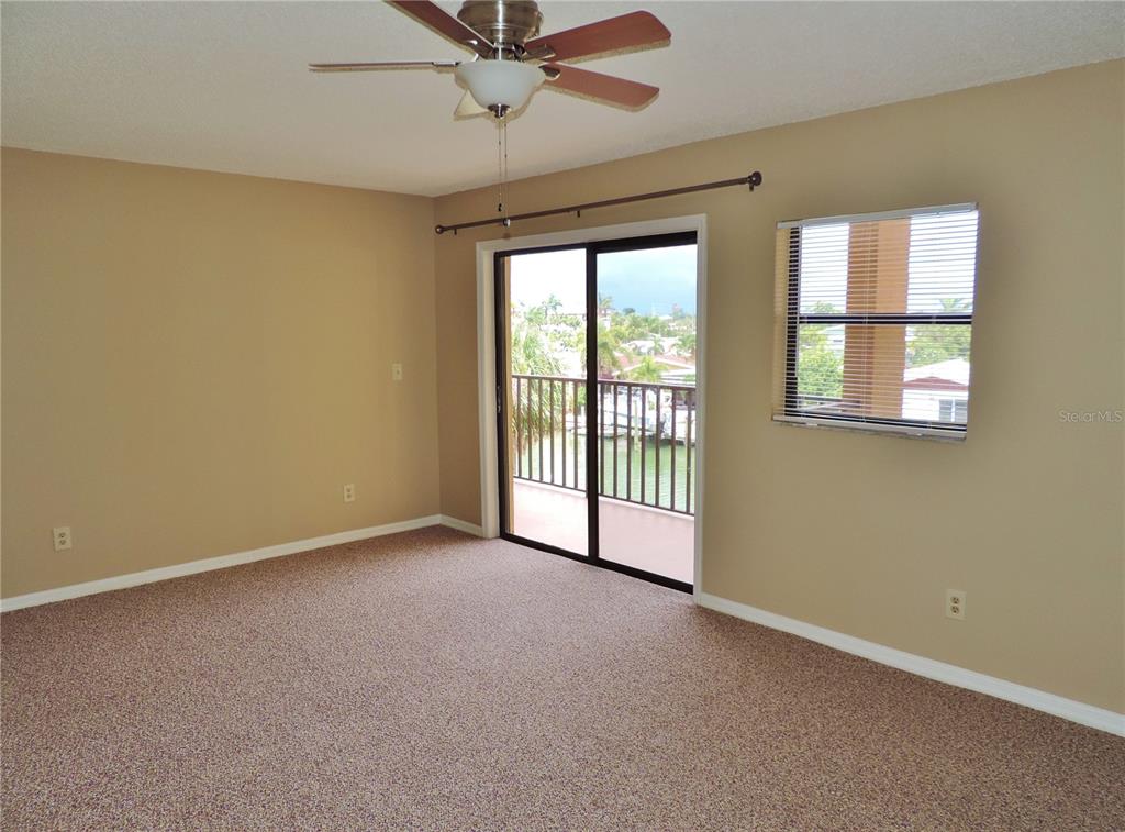 An empty bedroom features beige walls, brown carpet, a ceiling fan, and a sliding glass door — 145 116TH AVENUE UNIT 301, TREASURE ISLAND, FL