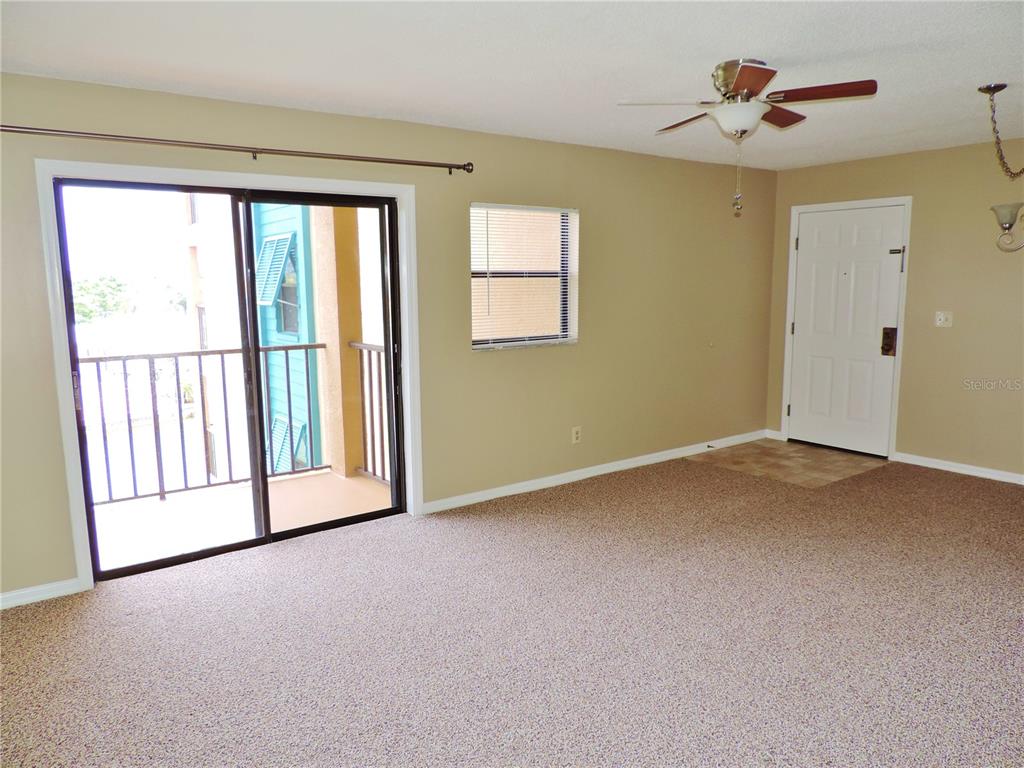 An empty living room features beige walls, tan carpeting, a ceiling fan, and a sliding door — 145 116TH AVENUE UNIT 301, TREASURE ISLAND, FL