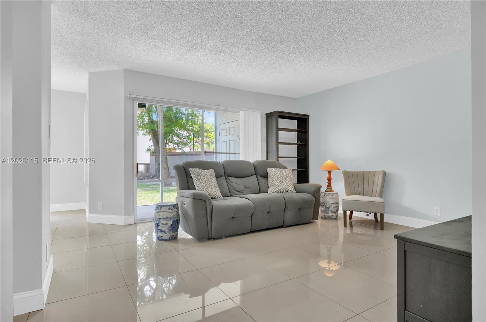 A living room features light-colored tile flooring, a gray sofa, and a sliding glass door — 13946 SW 91st Ter # 13946, Miami FL 33186, MIAMI, FL