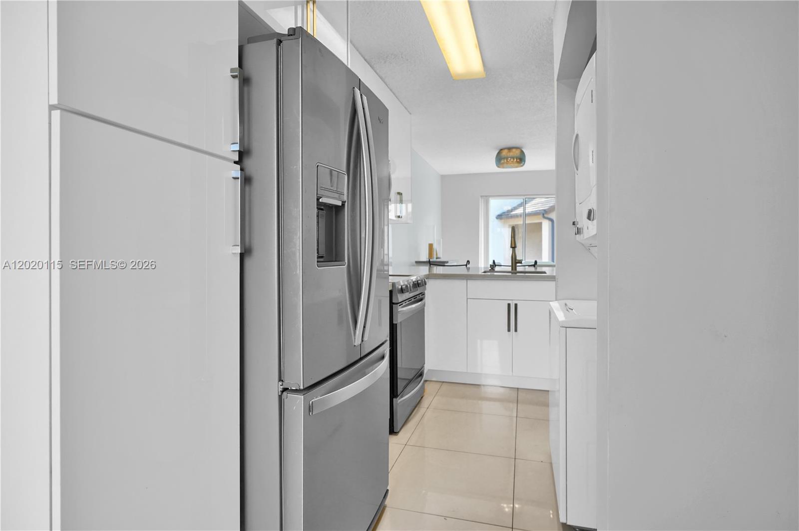 A galley-style kitchen features white cabinetry, stainless steel appliances, and light-colored tile flooring — 13946 SW 91st Ter # 13946, Miami FL 33186, MIAMI, FL