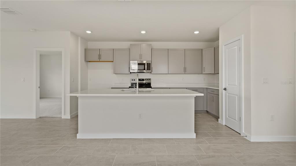 A modern kitchen features gray cabinets, a white quartz island, and light tile flooring — 816 ANDREW STREET, WINTER HAVEN, FL