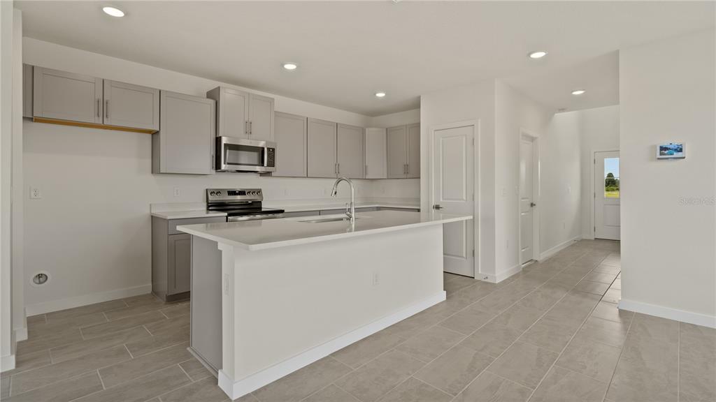 A modern kitchen features gray cabinetry, white countertops, a central island, and light tile flooring — 816 ANDREW STREET, WINTER HAVEN, FL