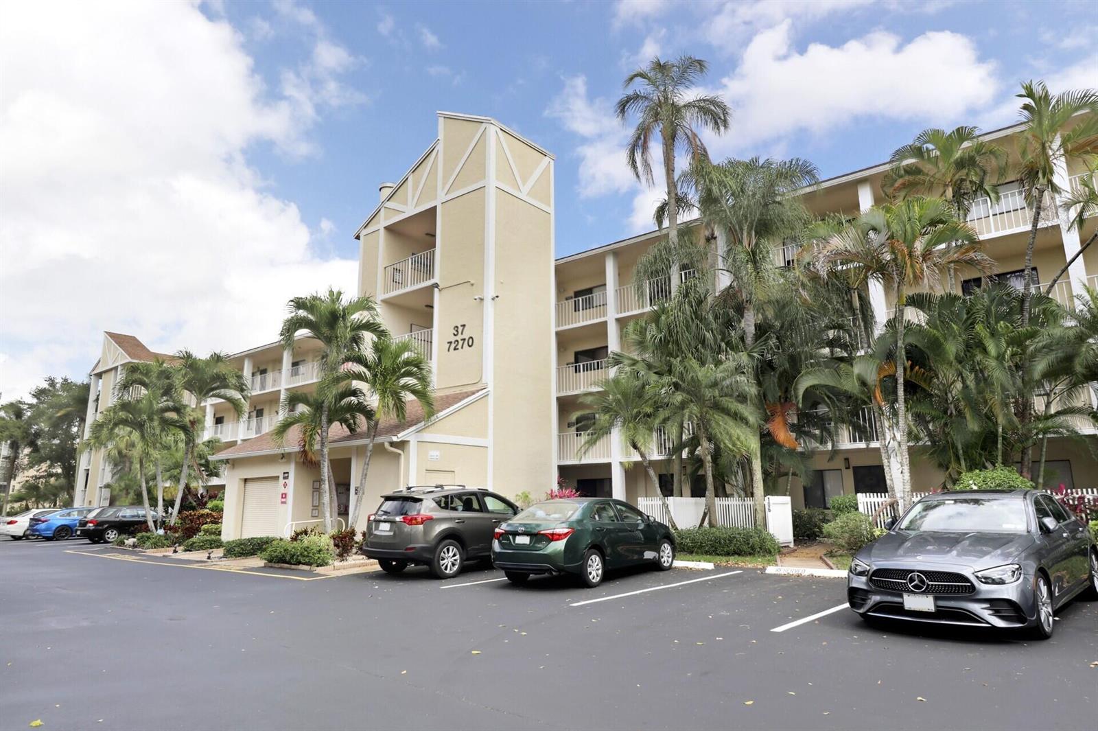 A multi-story apartment building with a parking lot and palm trees in front — 7270 Ashford Place # 106, Delray Beach FL 33446, DELRAY BEACH, FL