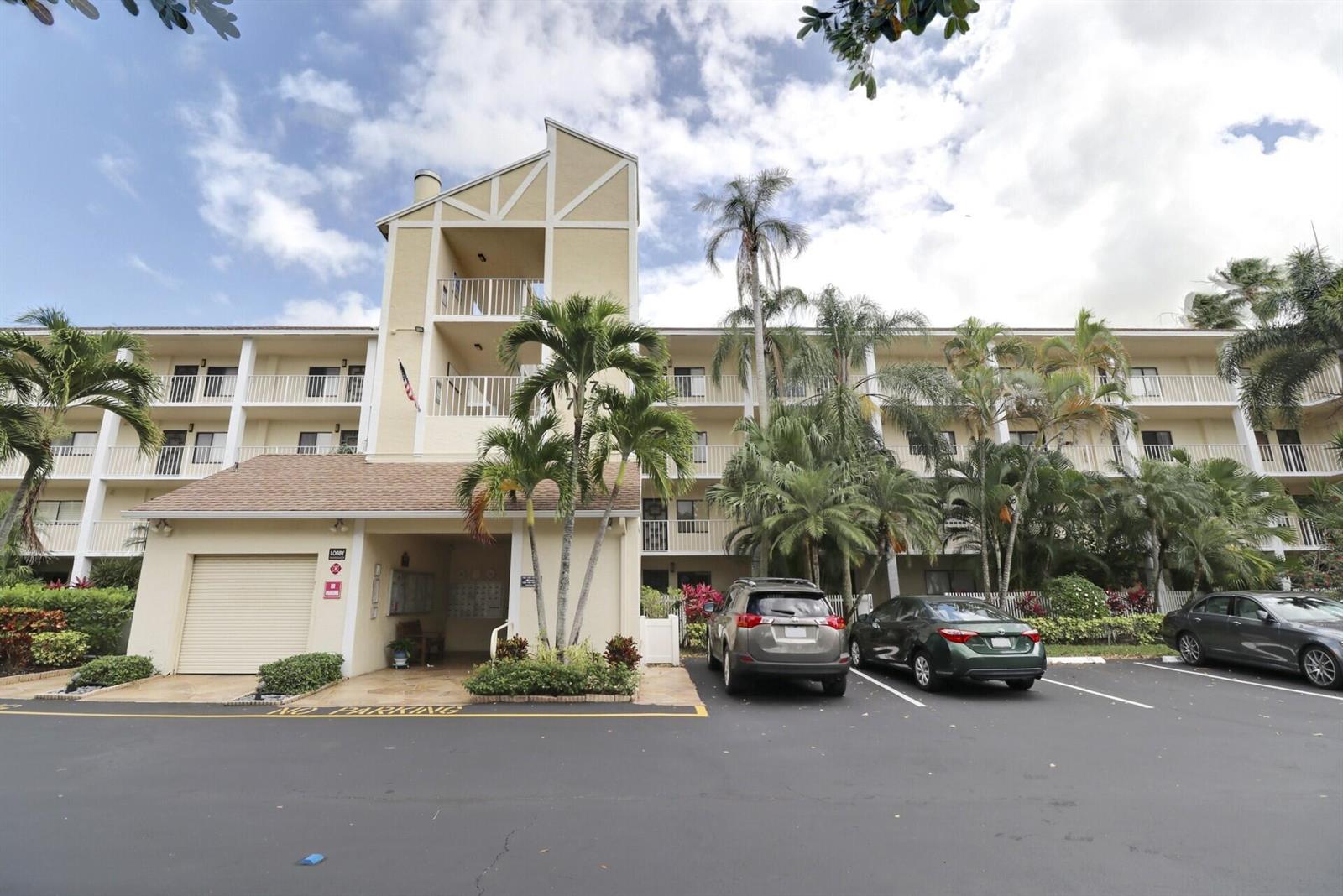 A multi-story apartment building with a beige exterior, palm trees, and a parking lot — 7270 Ashford Place # 106, Delray Beach FL 33446, DELRAY BEACH, FL