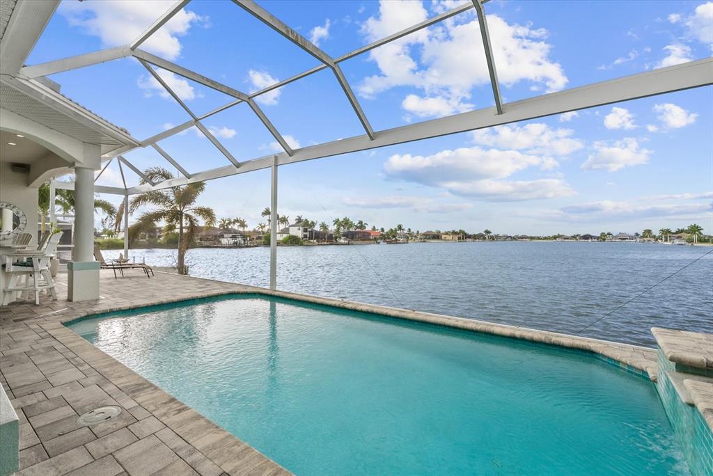 A screened-in patio features a swimming pool overlooking a large lake and distant houses — 4227 NW 28TH STREET, CAPE CORAL, FL
