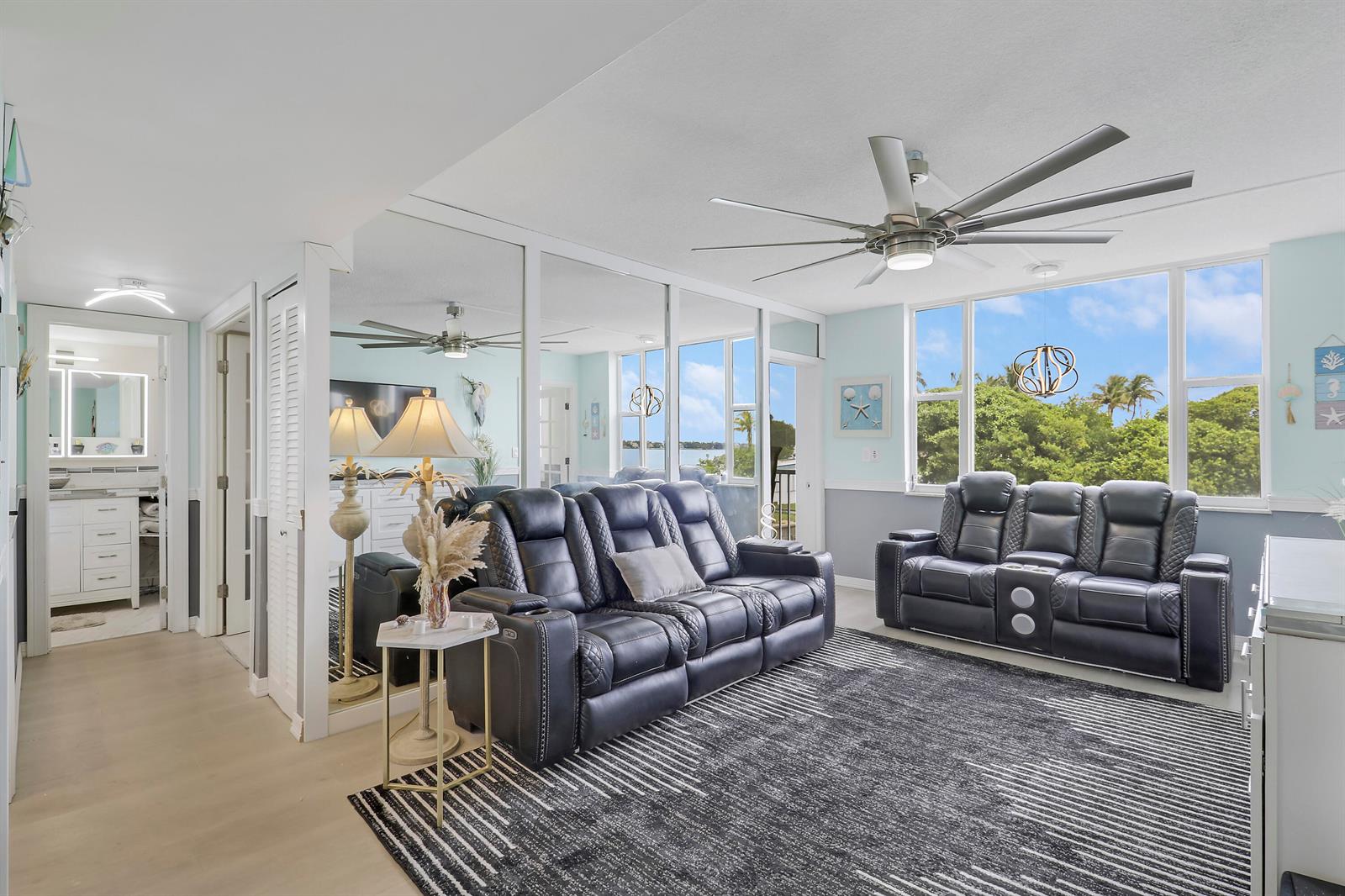 A living room features dark leather reclining sofas, a patterned rug, and large windows — 1820 New Palm Way # 202, Boynton Beach FL 33435, BOYNTON BEACH, FL