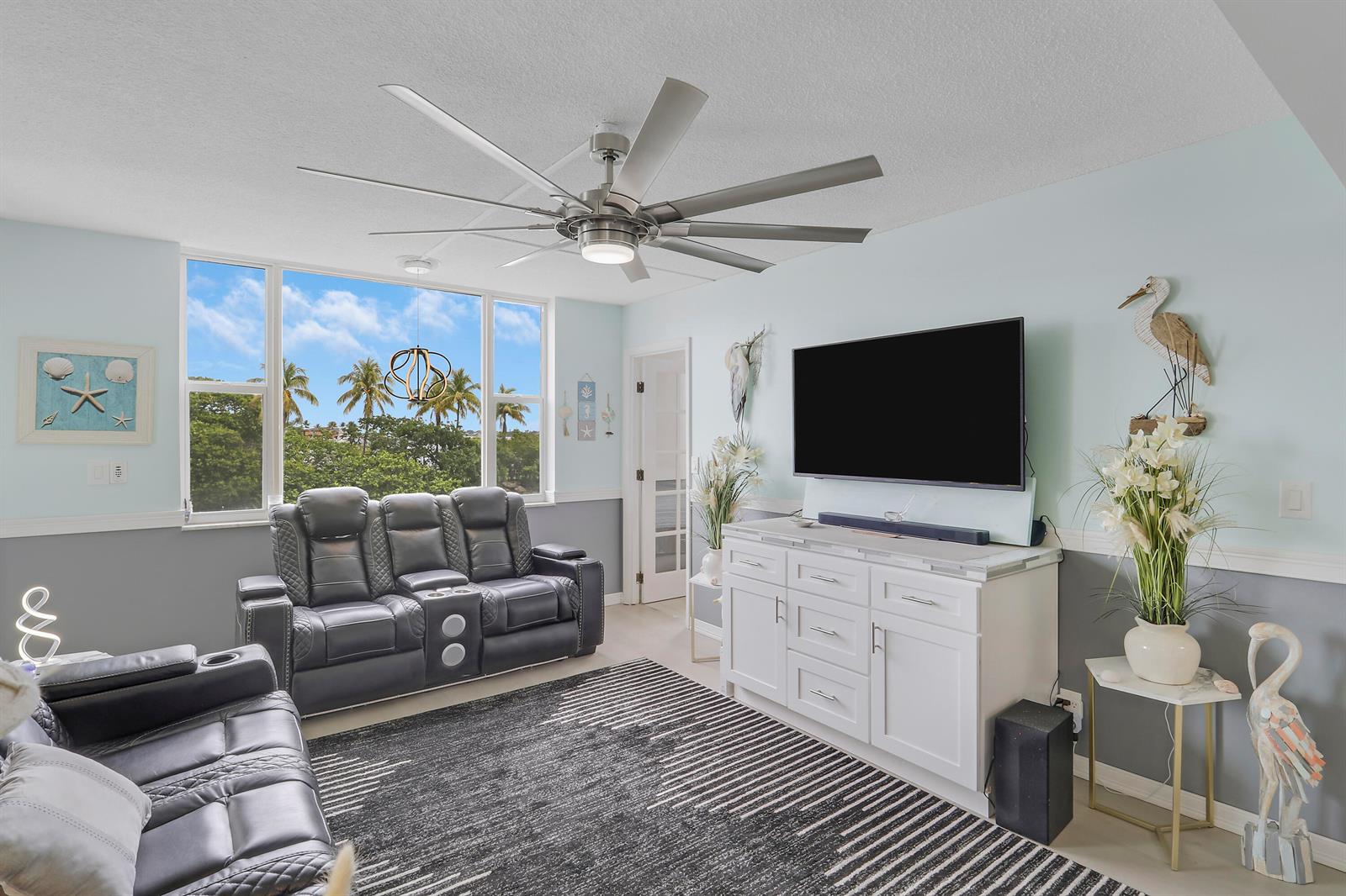 A living room features dark leather recliners, a large television, and a ceiling fan — 1820 New Palm Way # 202, Boynton Beach FL 33435, BOYNTON BEACH, FL