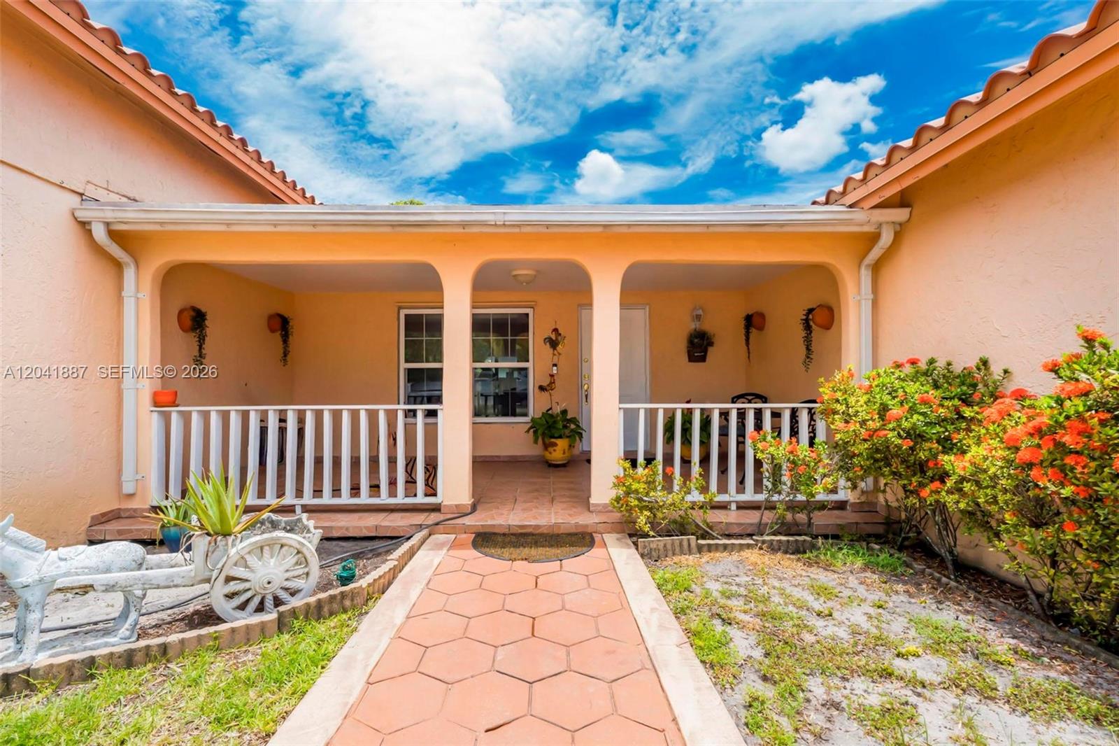A peach-colored house features a covered front porch with white railings and a tiled walkway — 19240 NW 60th Ct, Hialeah FL 33015, HIALEAH, FL