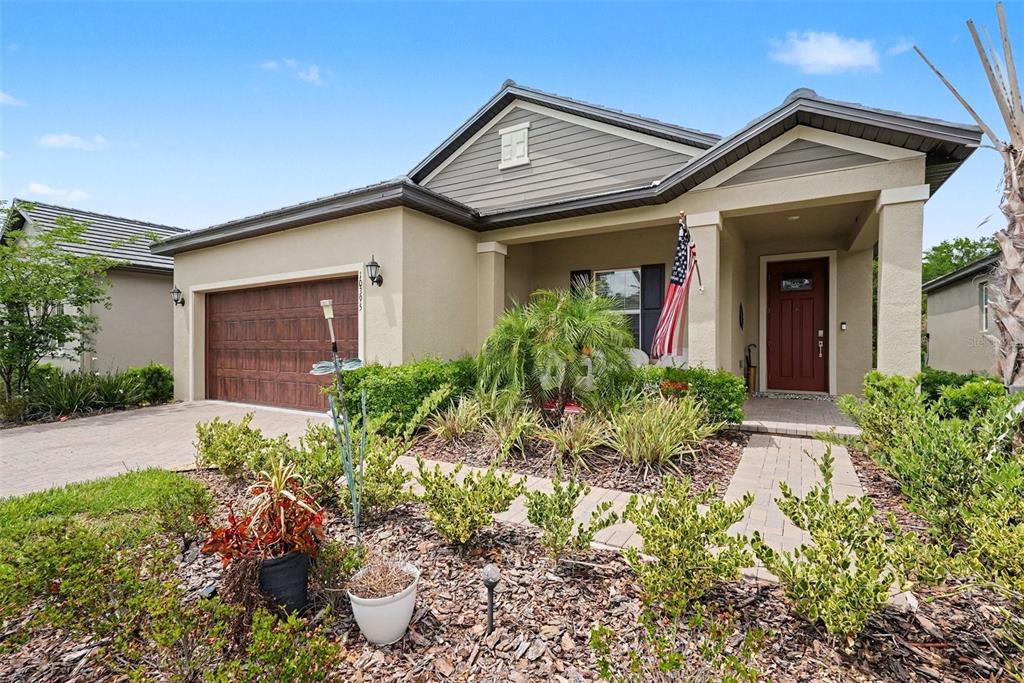 A single-story house with a tan stucco exterior, brown garage door, and a front porch — 10395 BANYAN BREEZE BOULEVARD, LAND O LAKES, FL