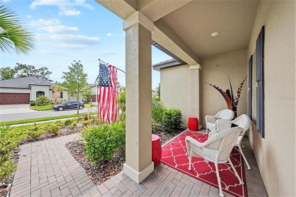 A covered front porch features a red rug, white wicker chairs, and a flag — 10395 BANYAN BREEZE BOULEVARD, LAND O LAKES, FL