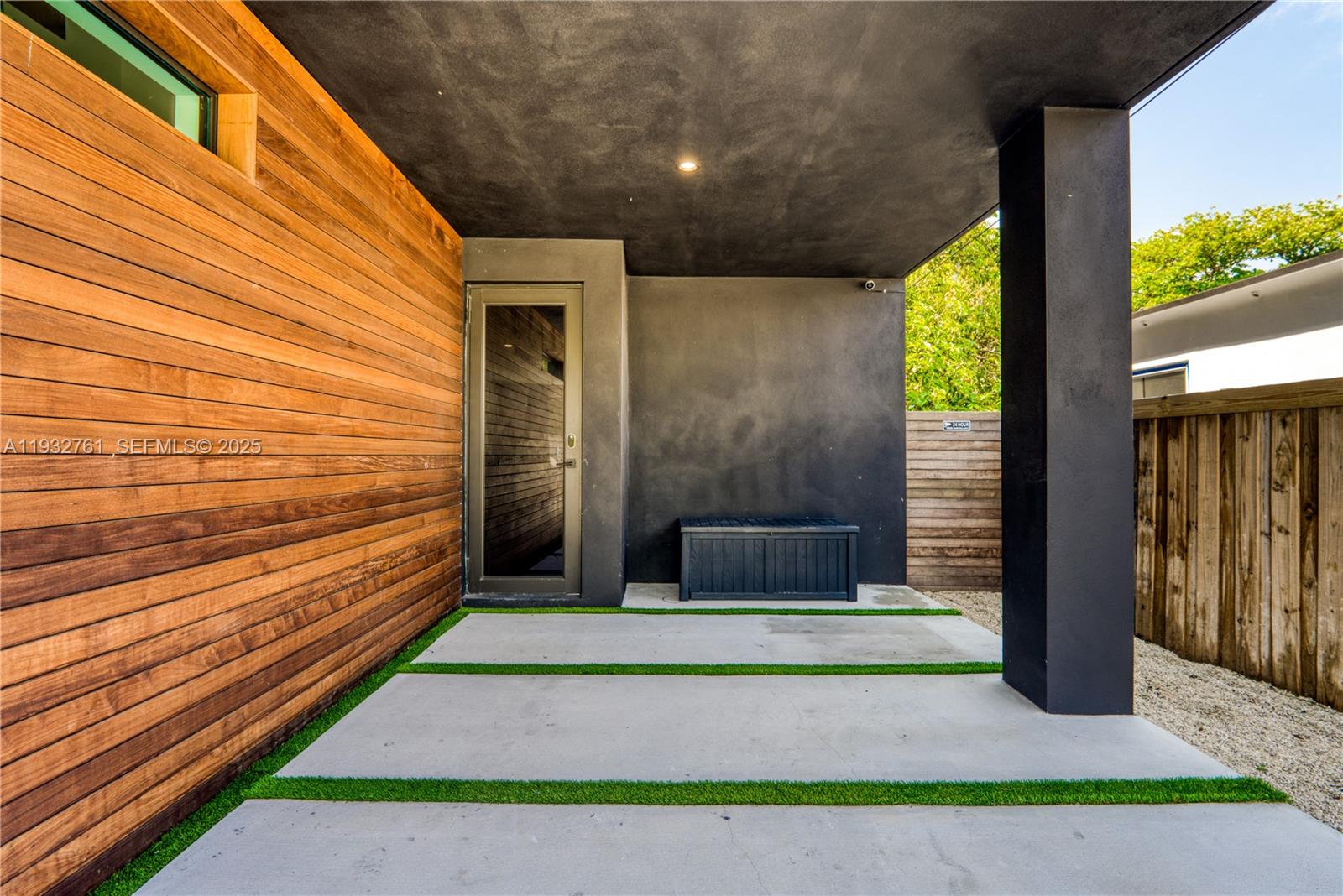 A modern covered entryway features wood siding, a black wall, and concrete pavers with grass — 58 NW 52nd St, Miami FL 33127, MIAMI, FL
