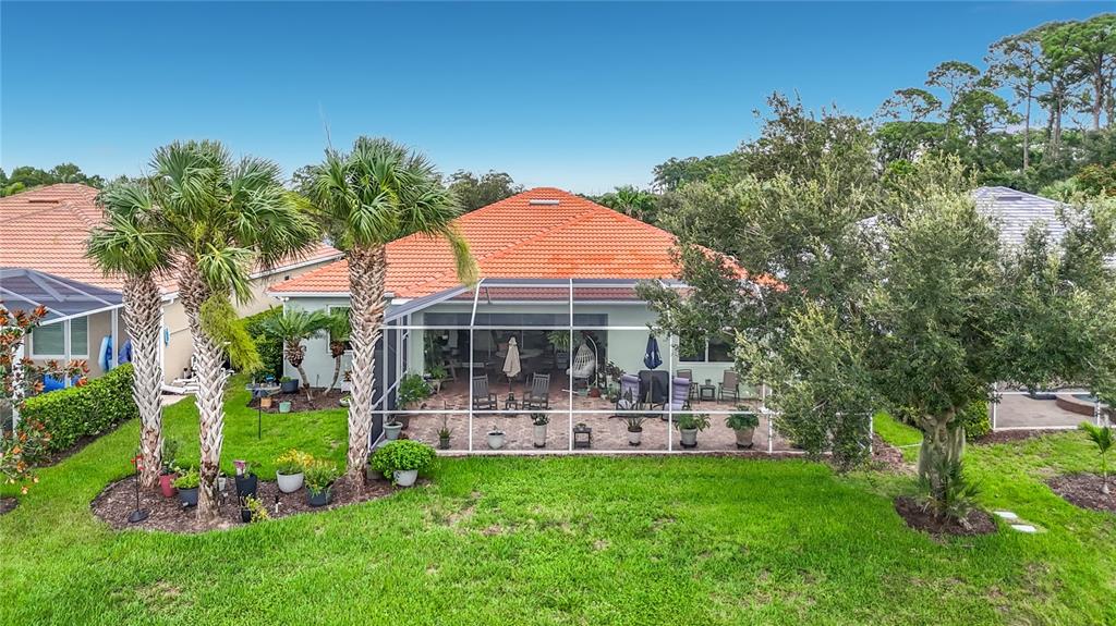 A rear view of a house with a screened-in patio, palm trees, and a lawn — 6149 ABACO DRIVE, SARASOTA, FL
