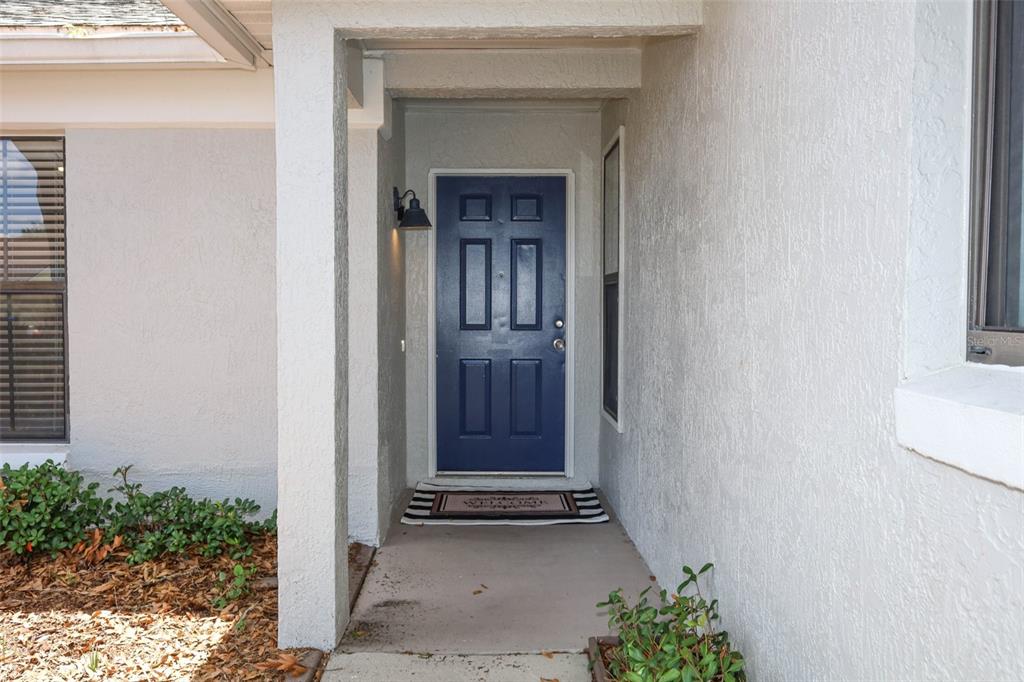 A blue front door is set within a covered entryway featuring light-colored stucco walls — 1047 ABELL CIRCLE, OVIEDO, FL