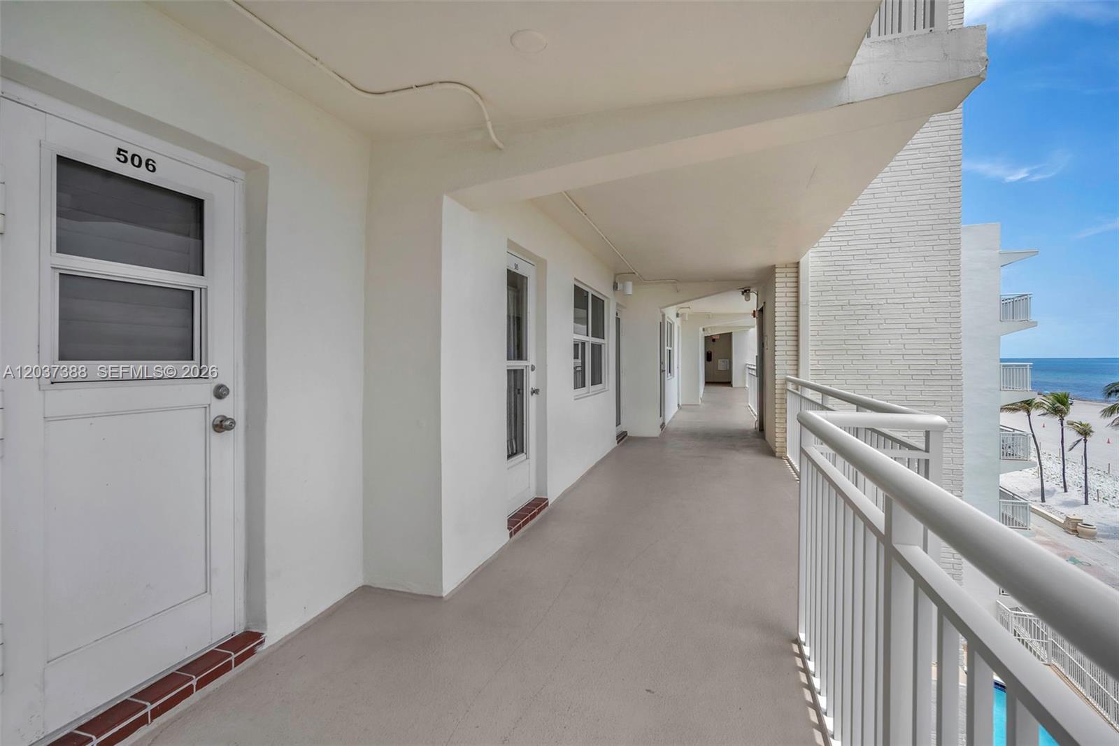 An outdoor apartment building walkway features white doors, a metal railing, and ocean views — 901 S Surf Rd # 506, Hollywood FL 33019, HOLLYWOOD, FL