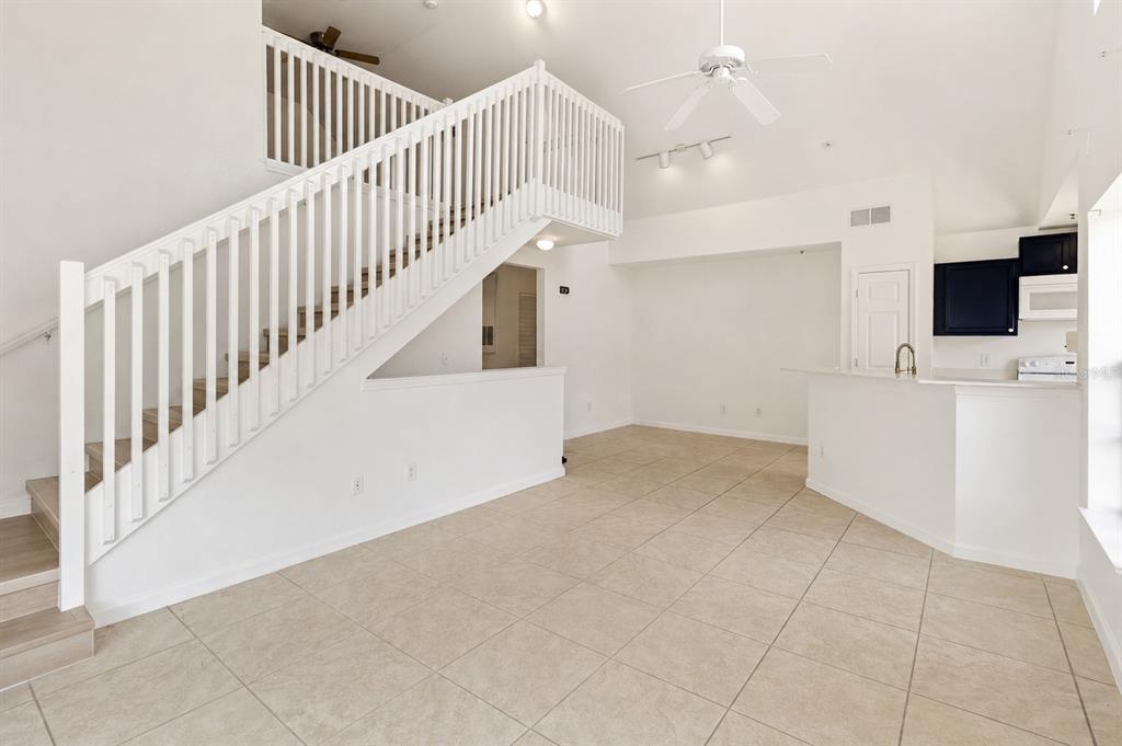 An open-concept living area features a white staircase, tile flooring, and a kitchen pass-through — 9157 LEE VISTA BOULEVARD UNIT 205, ORLANDO, FL