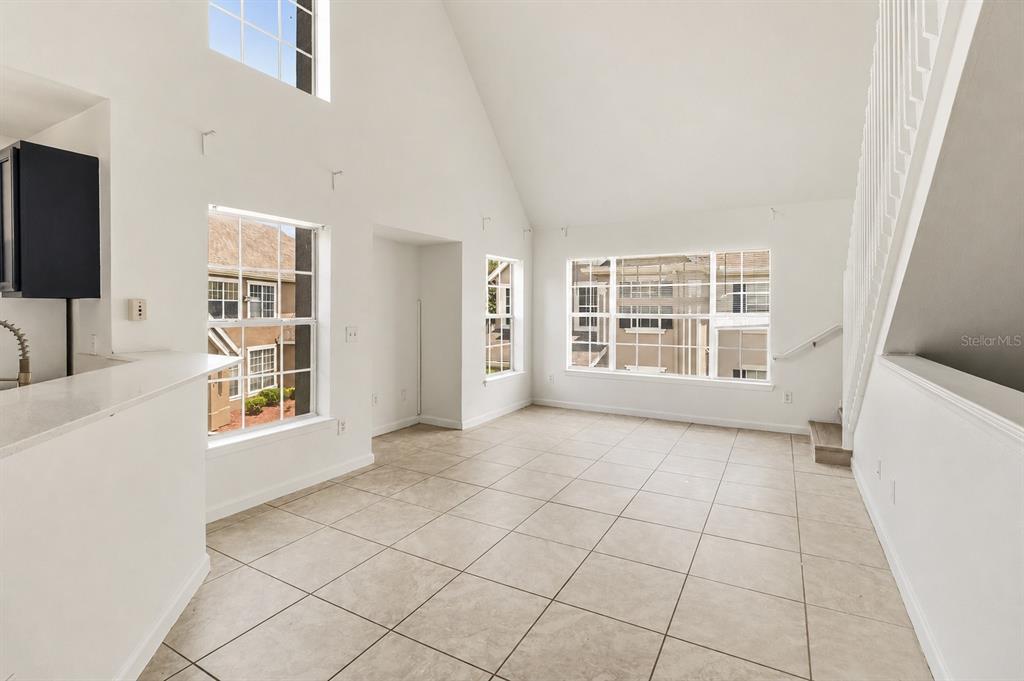 A bright living area features vaulted ceilings, large windows, and light-colored tile flooring — 9157 LEE VISTA BOULEVARD UNIT 205, ORLANDO, FL
