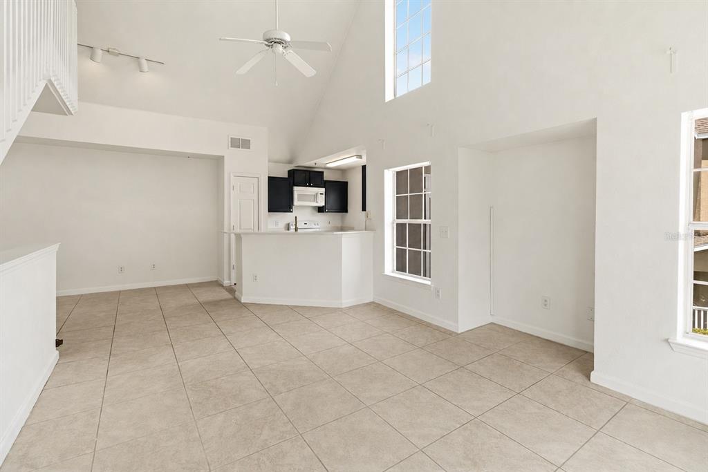 An open-concept living area with vaulted ceilings, tile flooring, and a kitchen with dark cabinets — 9157 LEE VISTA BOULEVARD UNIT 205, ORLANDO, FL