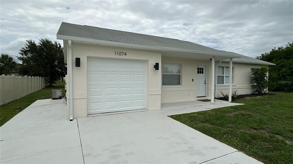 A single-story house with a white garage door, a front porch, and a concrete driveway — 11074 CARNEGIE AVENUE, ENGLEWOOD, FL