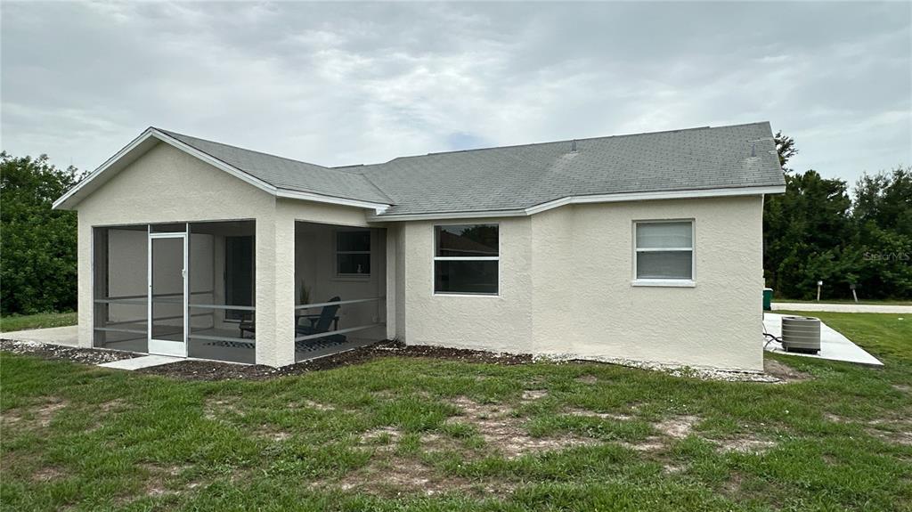 The rear exterior of a single-story house features a screened-in porch and two windows — 11074 CARNEGIE AVENUE, ENGLEWOOD, FL