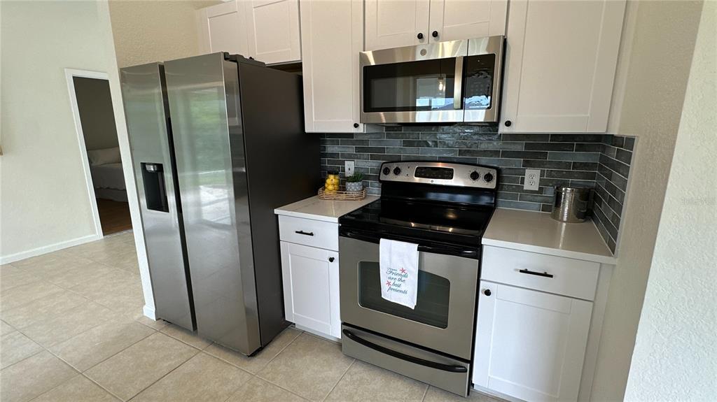 A kitchen features stainless steel appliances, white cabinets, and a gray tiled backsplash — 11074 CARNEGIE AVENUE, ENGLEWOOD, FL