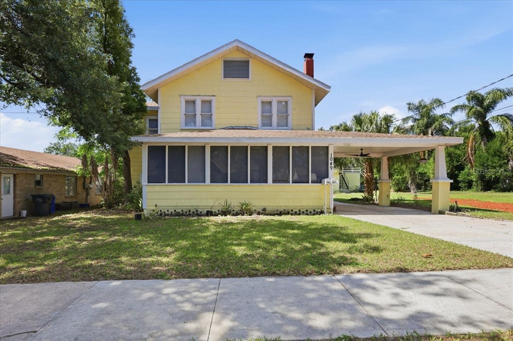 A yellow two-story house features a screened-in front porch and an attached carport — 1049 MONROE STREET, LAKELAND, FL