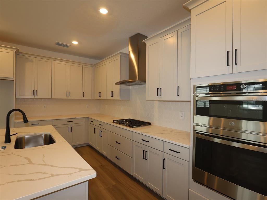 A modern kitchen features white cabinetry, quartz countertops, a gas cooktop, and stainless steel appliances — 4454 SUNSET GARDEN STREET, BRADENTON, FL