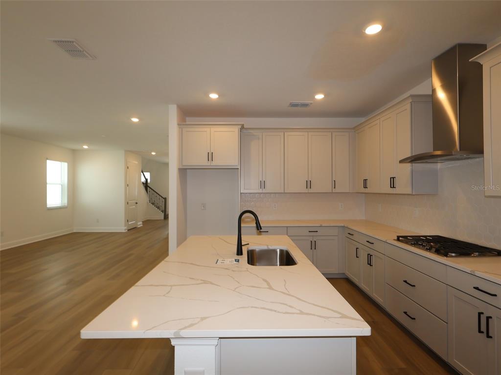A modern kitchen features light gray cabinets, a quartz island with a sink, and wood flooring — 4454 SUNSET GARDEN STREET, BRADENTON, FL