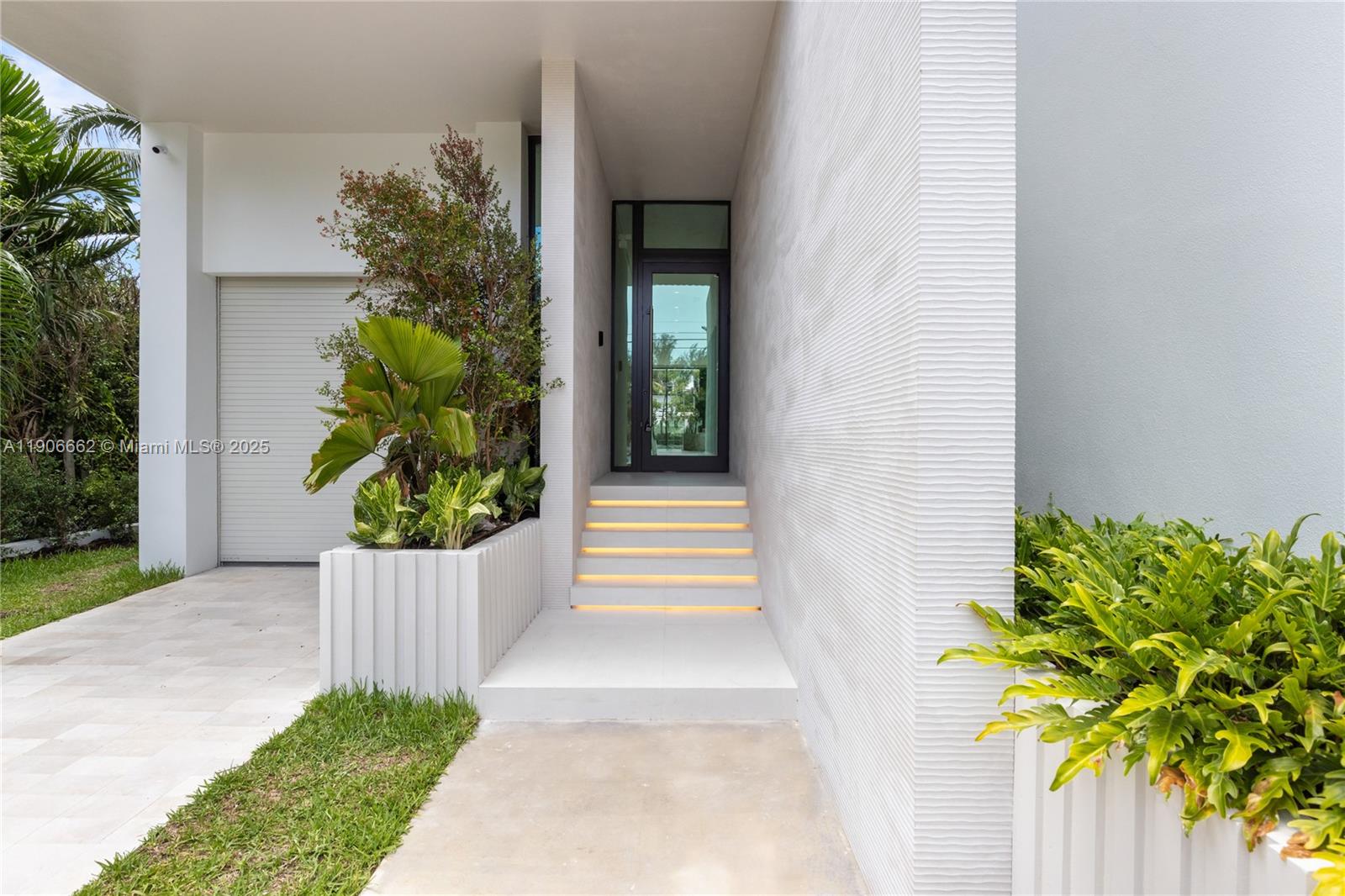 A modern home entrance features a glass door, illuminated steps, and textured white walls — 4504 Sheridan Ave, Miami Beach FL 33140, MIAMI BEACH, FL