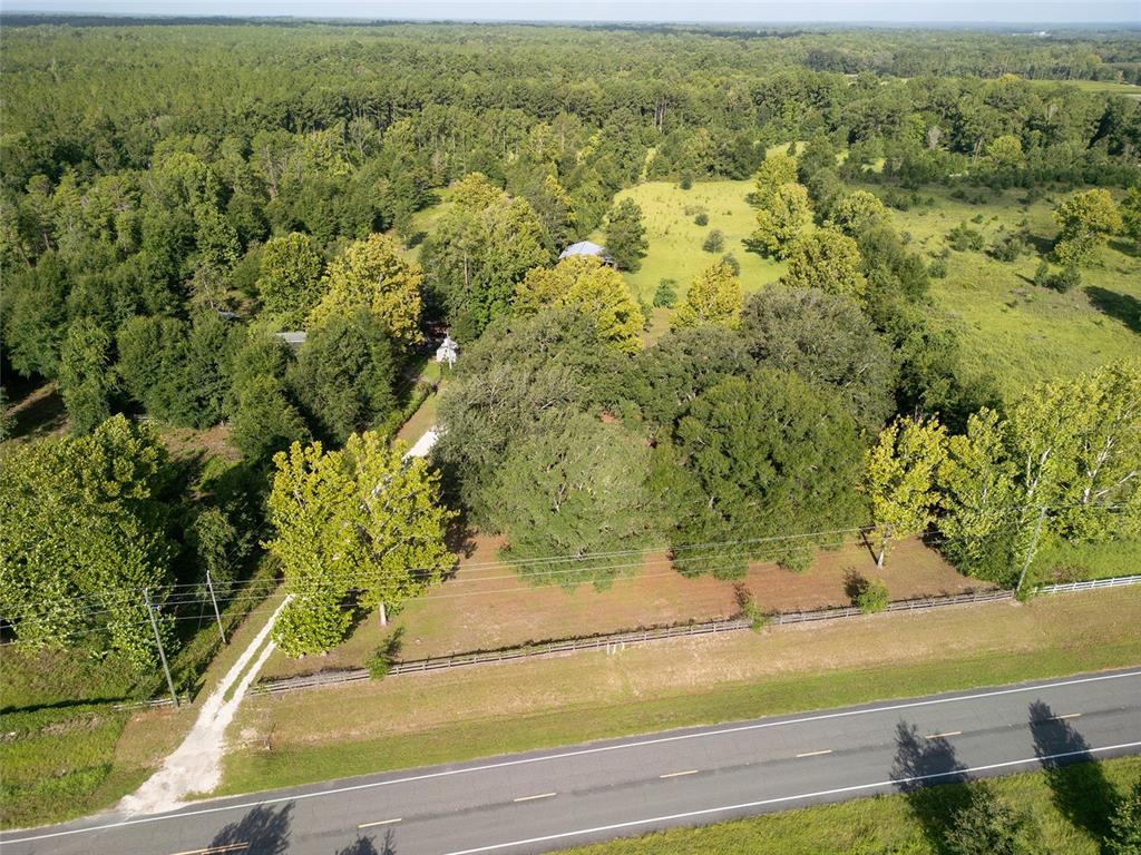 An aerial view shows a house nestled among trees behind a fenced yard and road — 25518 NW COUNTY ROAD 241, ALACHUA, FL