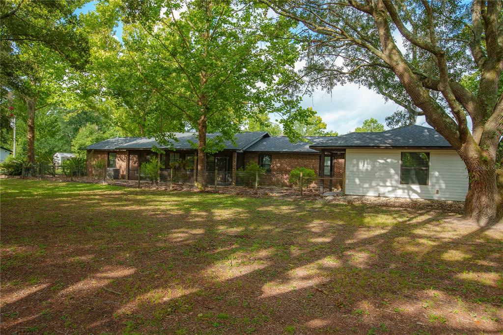 A brick house with a white-sided addition sits behind a wire fence in a yard — 25518 NW COUNTY ROAD 241, ALACHUA, FL