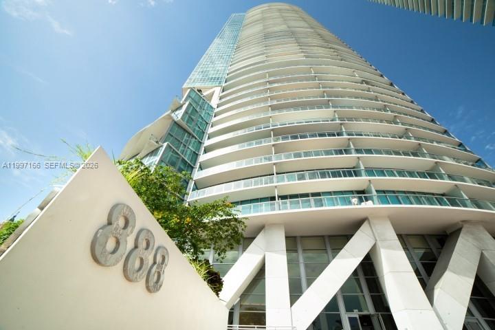 A low-angle view of a modern high-rise residential building with a prominent address sign — 888 Biscayne Blvd # 2211, Miami FL 33132, MIAMI, FL