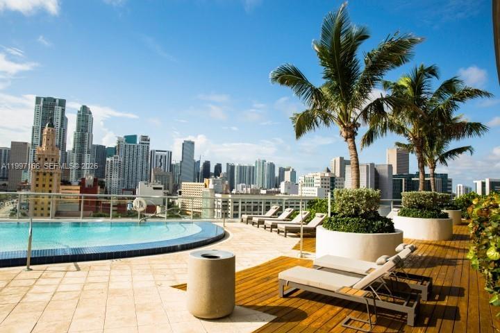 A rooftop pool deck overlooks a city skyline with lounge chairs and palm trees — 888 Biscayne Blvd # 2211, Miami FL 33132, MIAMI, FL