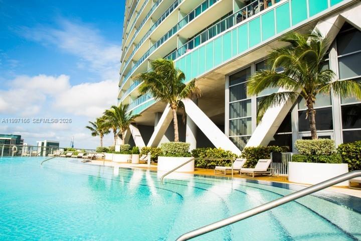 A swimming pool sits on a terrace beneath a modern high-rise building with palm trees — 888 Biscayne Blvd # 2211, Miami FL 33132, MIAMI, FL