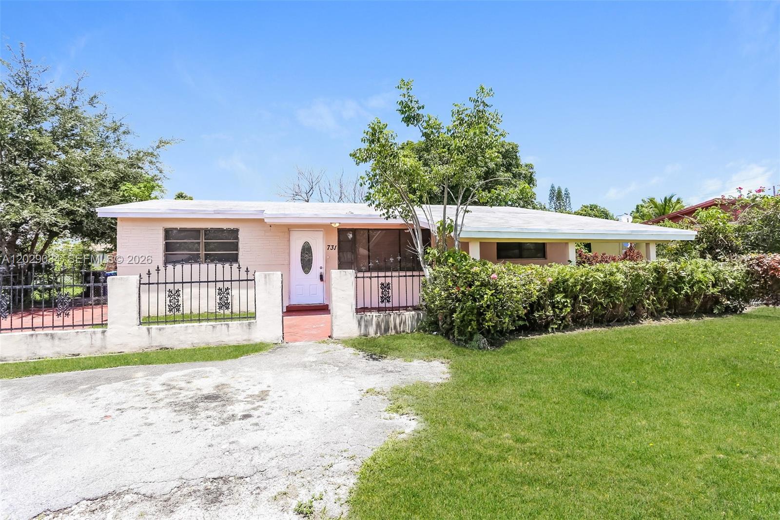 A single-story peach-colored house features a white front door, metal fencing, and a grassy yard — 731 NW 175th Dr, Miami Gardens FL 33169, MIAMI GARDENS, FL