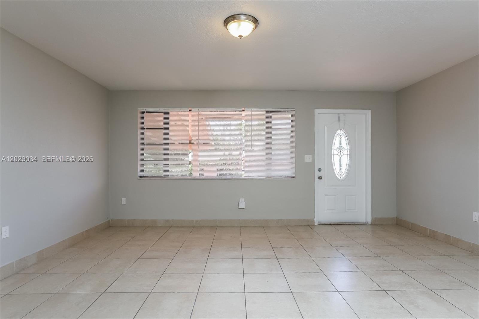 An empty room features light-colored tile flooring, gray walls, a window with blinds, and a door — 731 NW 175th Dr, Miami Gardens FL 33169, MIAMI GARDENS, FL