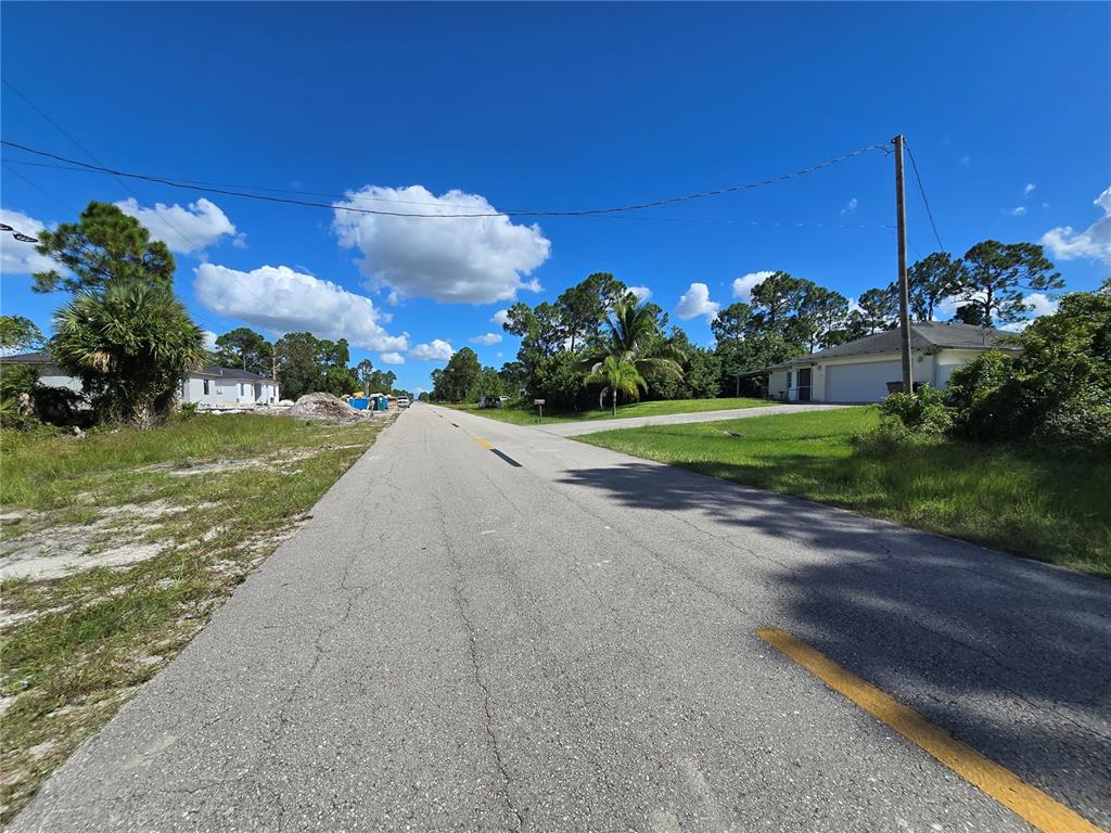 A paved road stretches between grassy lots with houses and trees under a blue sky — 1111 NIMITZ BOULEVARD, LEHIGH ACRES, FL