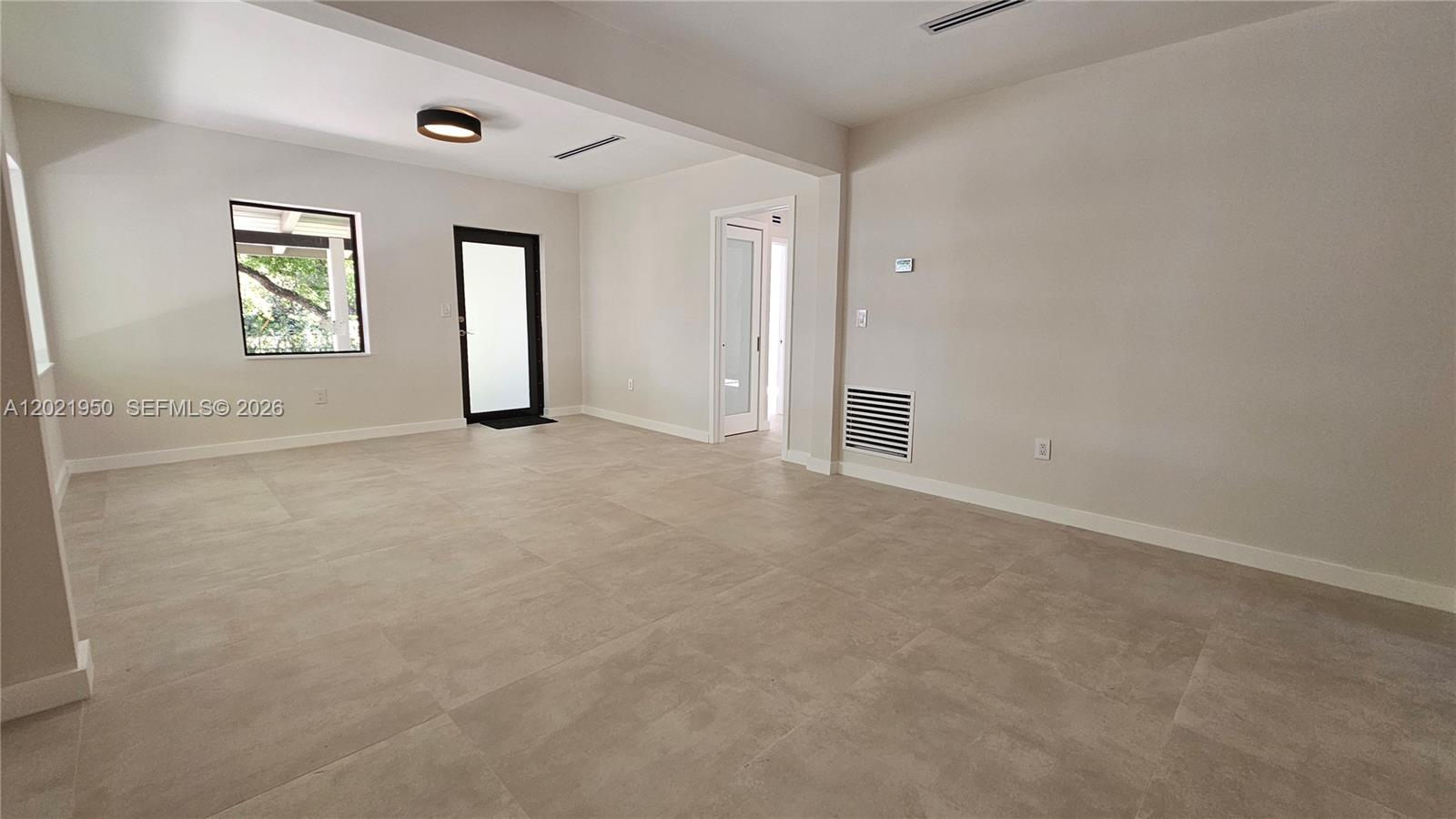 An empty room features light-colored tile flooring, neutral walls, a black-framed door, and recessed lighting — 424 NE 63rd St, Miami FL 33138, MIAMI, FL
