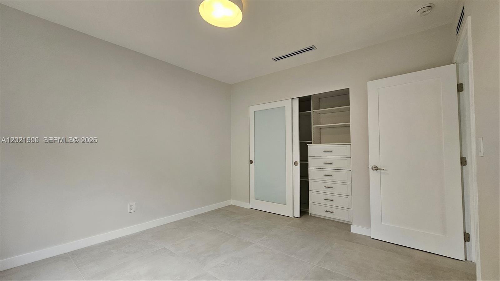 A room with light gray walls, tile flooring, a sliding closet door, and a white door — 424 NE 63rd St, Miami FL 33138, MIAMI, FL