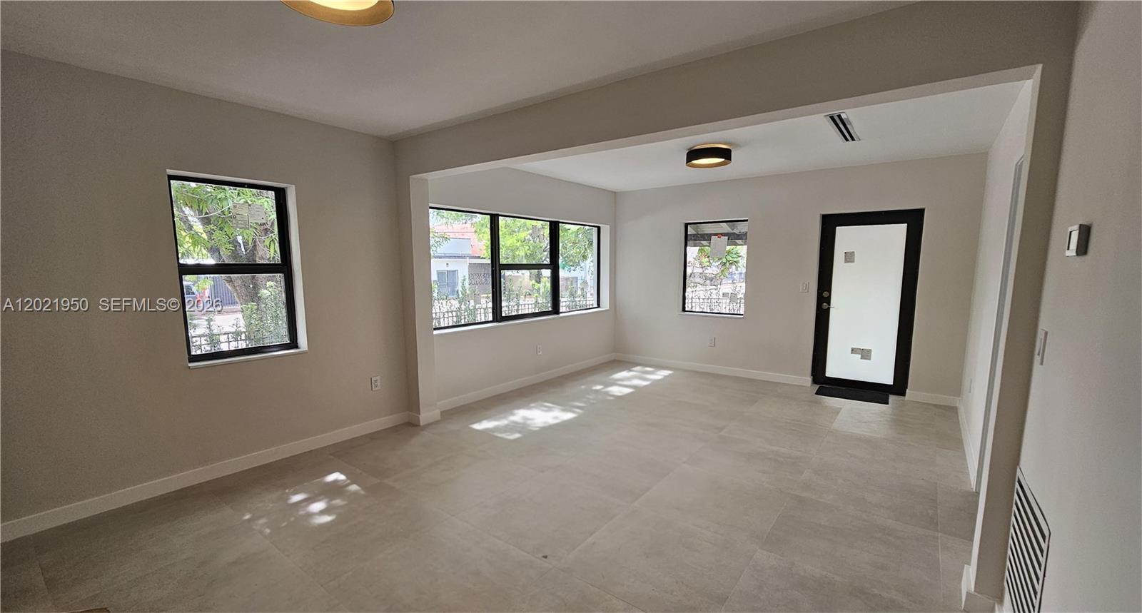 An empty room features light-colored tile flooring, neutral walls, large windows, and a black-framed door — 424 NE 63rd St, Miami FL 33138, MIAMI, FL
