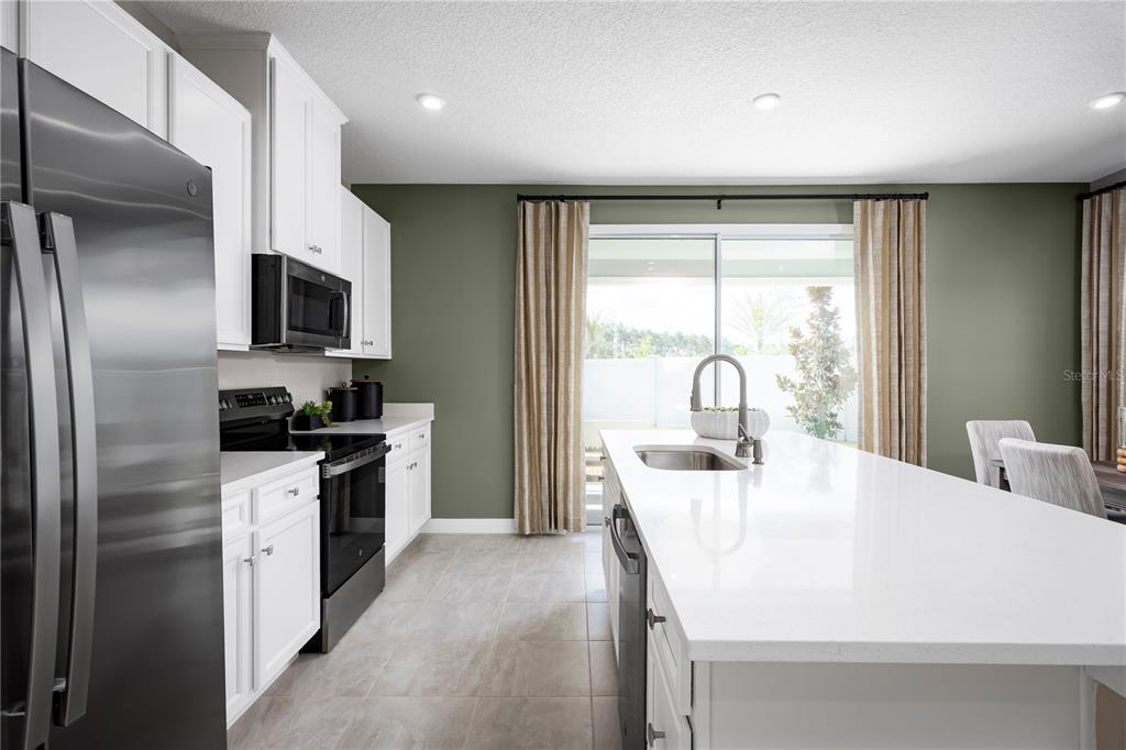 A modern kitchen features white cabinets, stainless steel appliances, a large island, and sliding doors — 3974 ADDIE WAY, MELBOURNE, FL