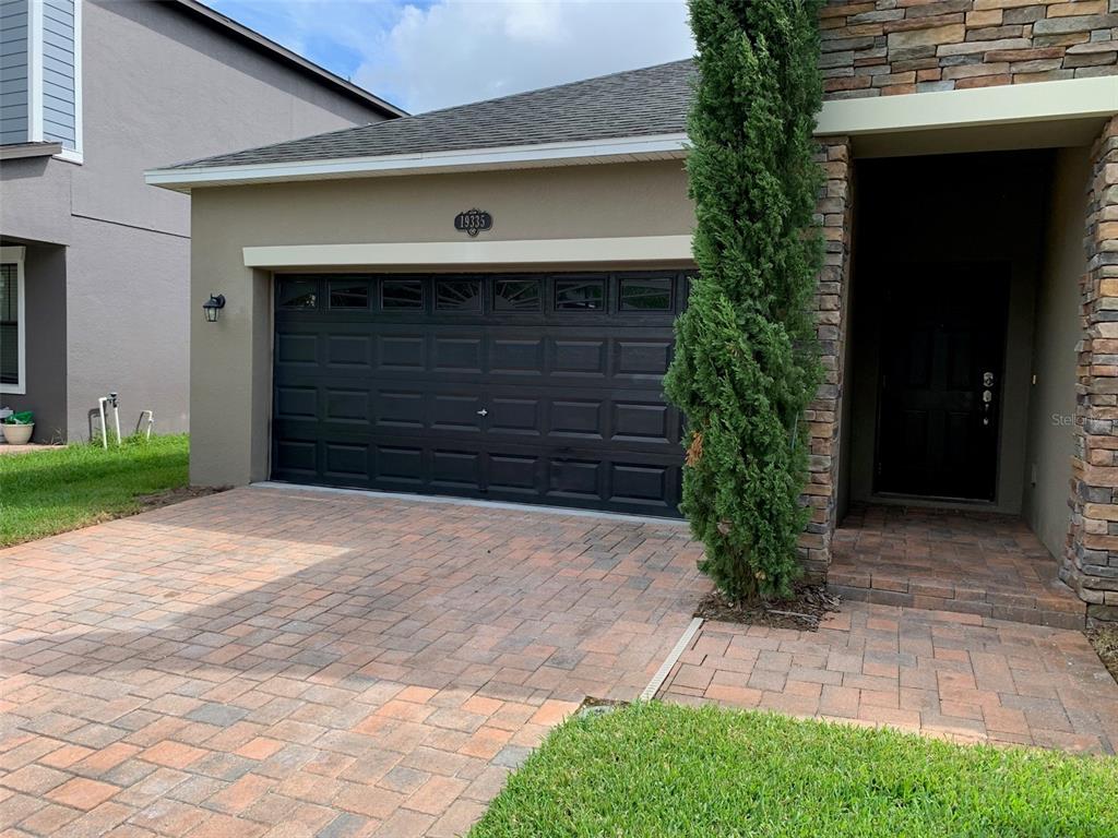 A paved driveway leads to a black garage door and a stone-accented entryway — 19335 PADDOCK VIEW DRIVE, TAMPA, FL