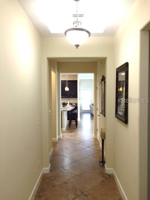 A hallway with tile flooring leads toward a kitchen with dark cabinets and a pendant light — 19335 PADDOCK VIEW DRIVE, TAMPA, FL