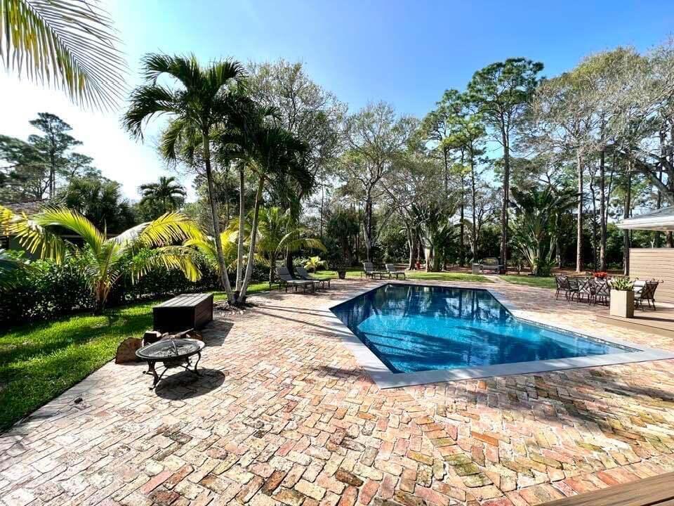 A rectangular swimming pool sits on a brick patio surrounded by palm trees and landscaping — 14256 Greentree Trail, Wellington FL 33414, WELLINGTON, FL