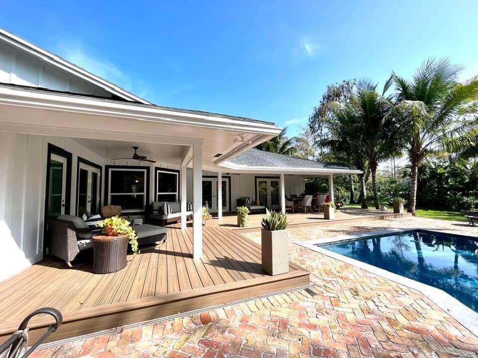 A covered wooden deck overlooks a swimming pool and a brick patio beside a house — 14256 Greentree Trail, Wellington FL 33414, WELLINGTON, FL
